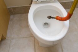 Plumber's snake unclogging a toilet in a residential home